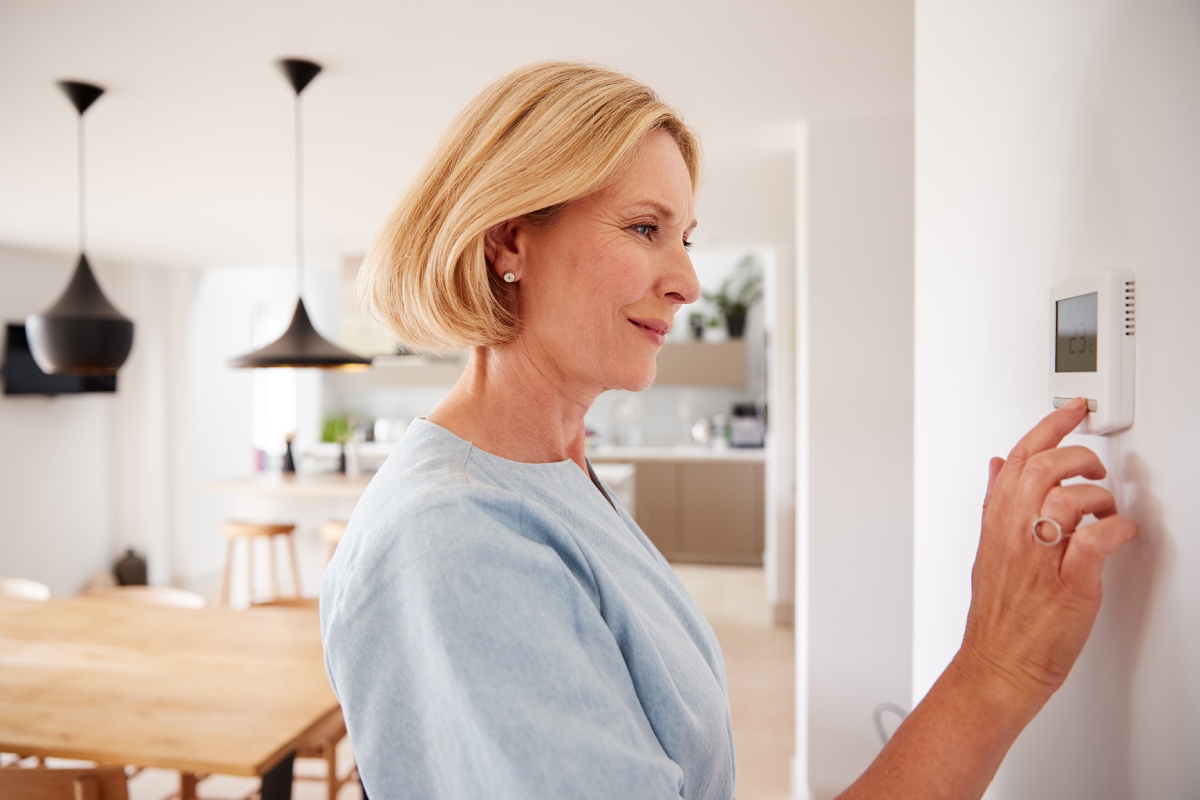 older woman adjusting the thermostat in her home