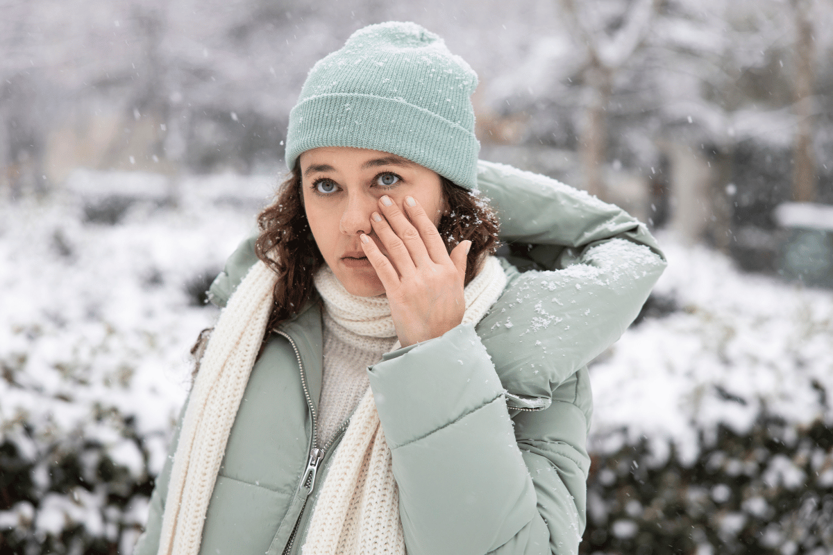 a woman standing outside in winter touching her eye due to discomfort