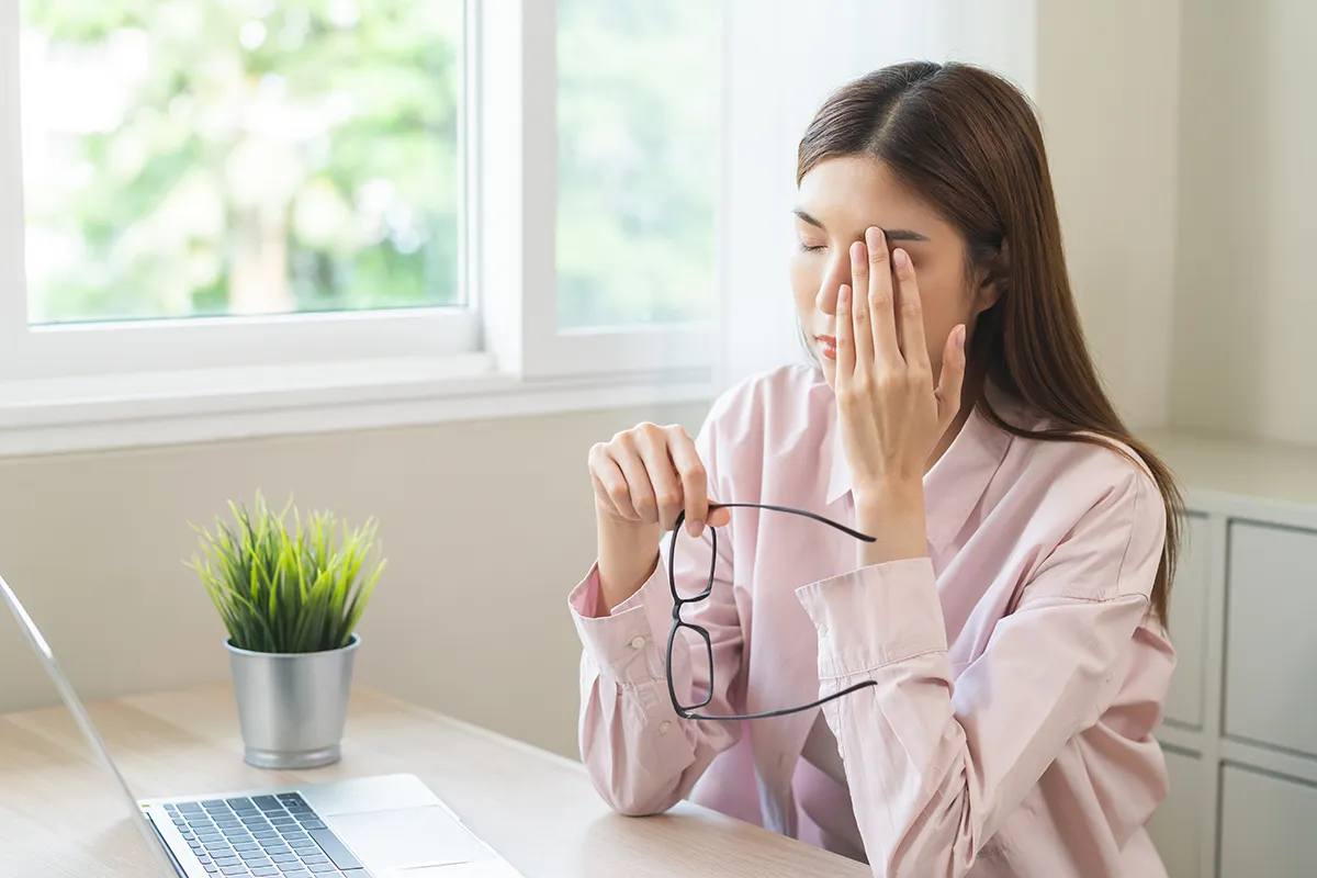 a young woman taking off her glasses and holding a hand to her eye in discomfort